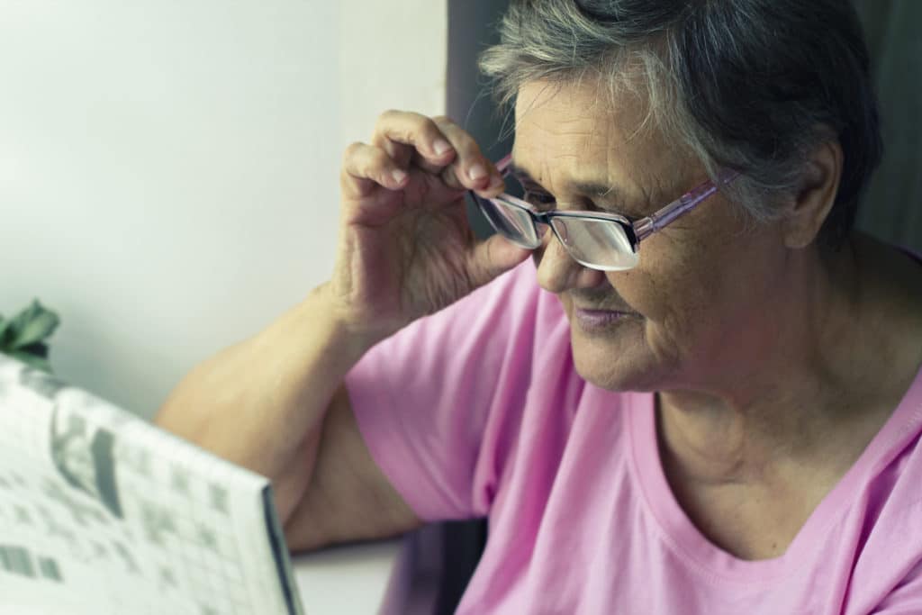 Une dame agée tient ses lunette en lisant le journal