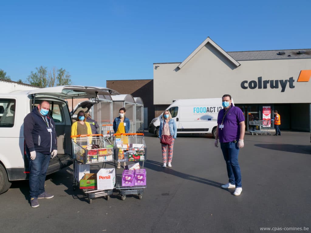 Cinq personnes devant le magasin Colruyt avec deux caddys remplis de courses